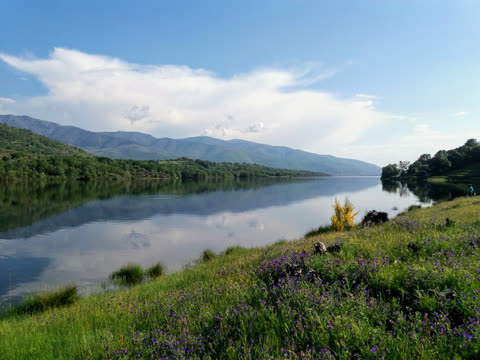 vista del pantano de baños de montemayor con las orillas verdes y con flores y las montañas reflejadas en el agua